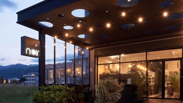 A modern building with a glass facade, circular cutouts on the exterior, and a sign that reads "noir". - noir B&B (Toucheng)