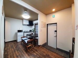 A compact kitchen with white cabinets, a microwave, a toaster, and a sink. There's a dining table with chairs and a potted plant. - Hana Botan (Kyoto)