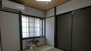 A traditional Japanese room with tatami flooring, a shoji screen window, and a dark sliding door. - Hana Botan (Kyoto)