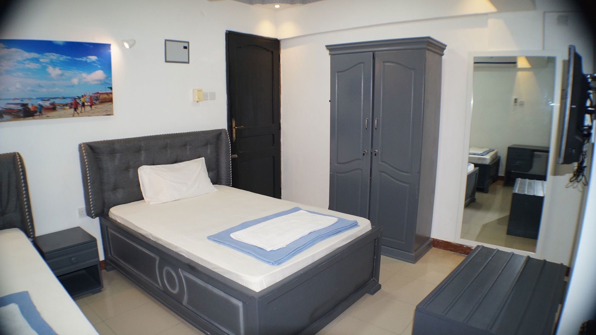 A bedroom with a bed, a wardrobe, a desk, and a mirror.