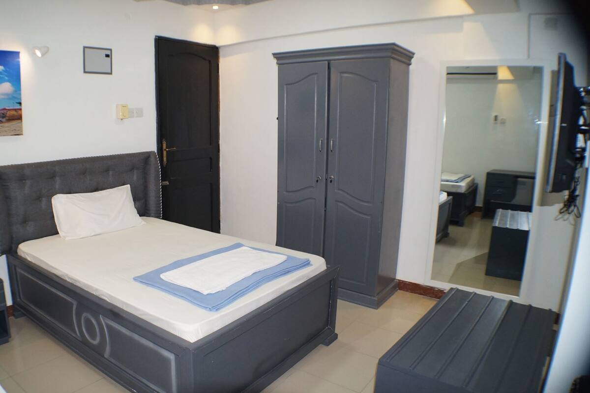 A bedroom with a bed, a wardrobe, a desk, and a mirror.