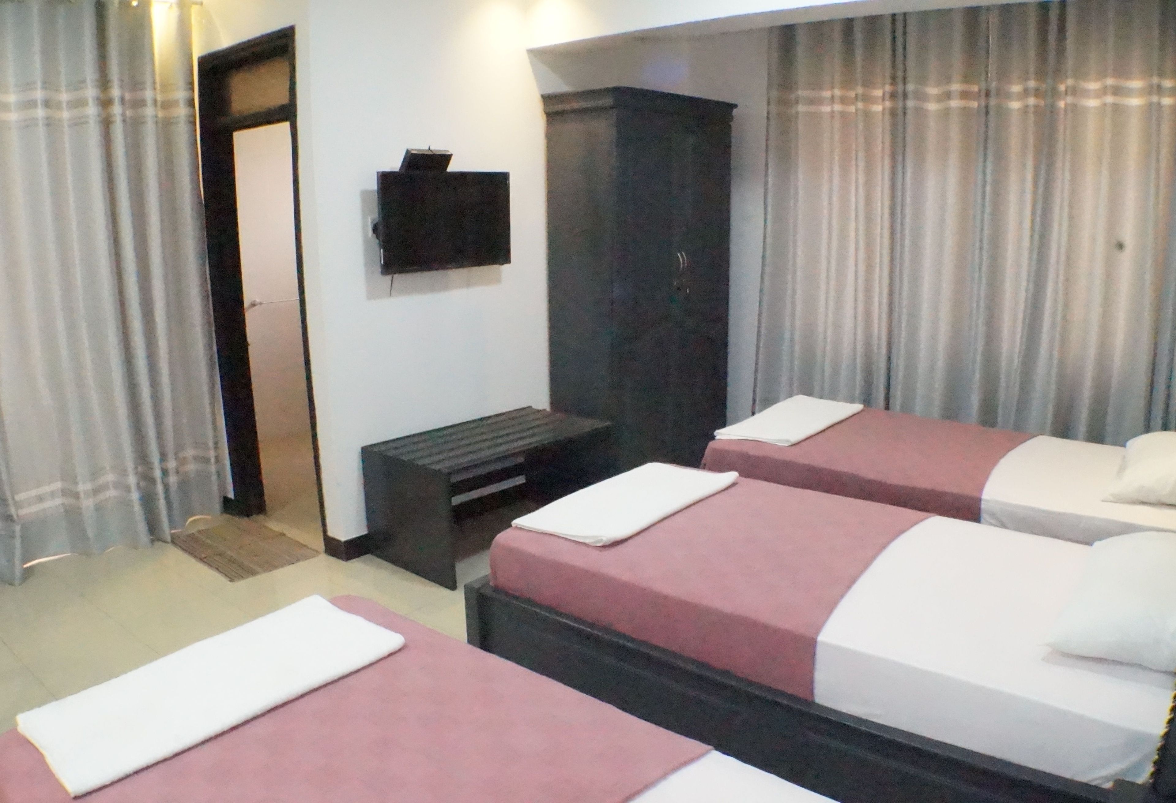 Hotellihuone, jossa on kolme sänkyä, seinälle asennettu televisio ja vaatekaappi.