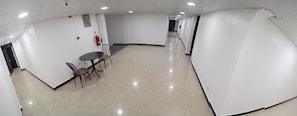A hallway with white walls, a tiled floor, and a table with chairs. There are fire extinguishers and a fire alarm on the walls. - Econo Lodge (Dar es Salaam)