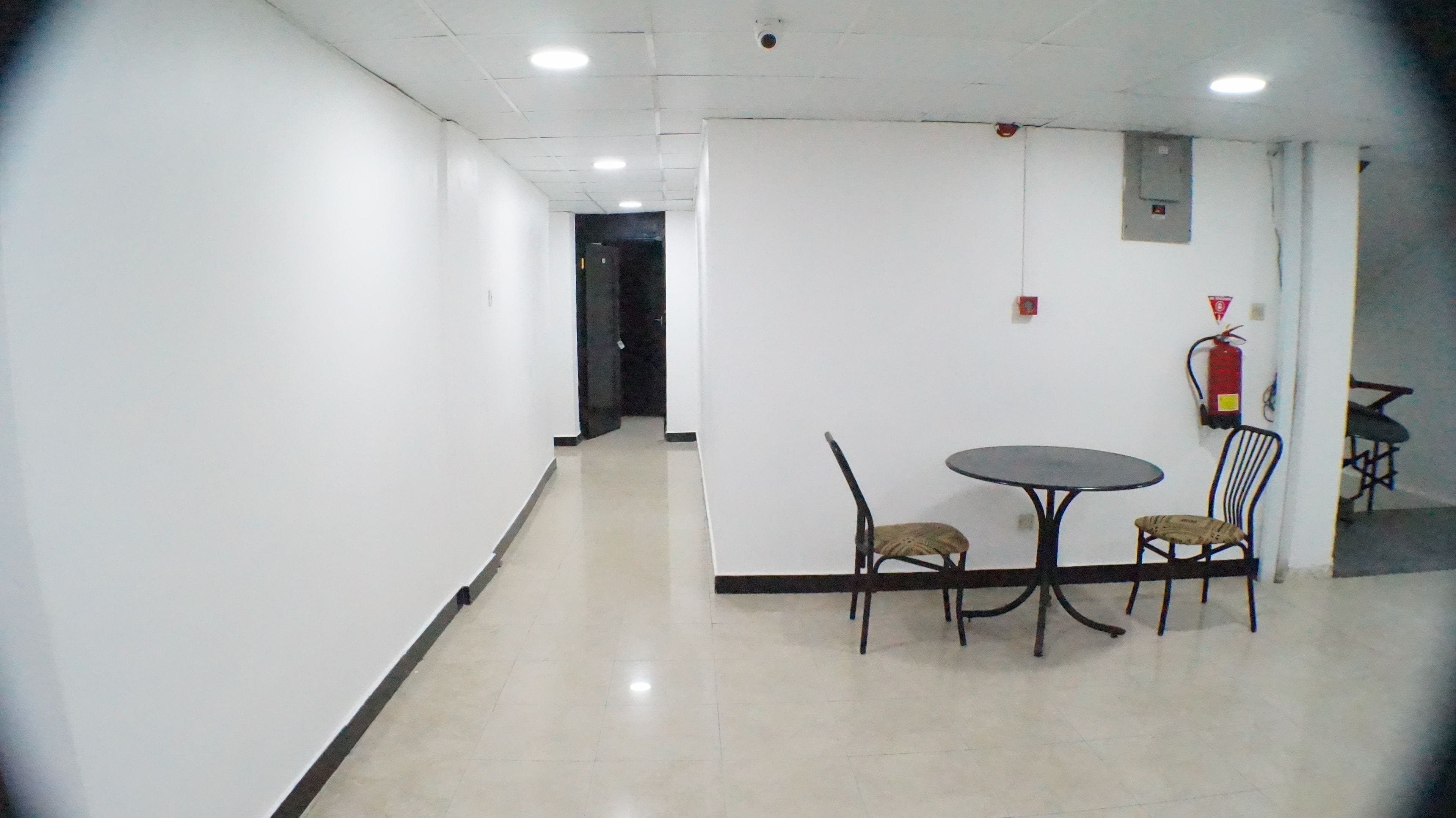 A hallway with a table and chairs, a fire extinguisher, and a door at the end.