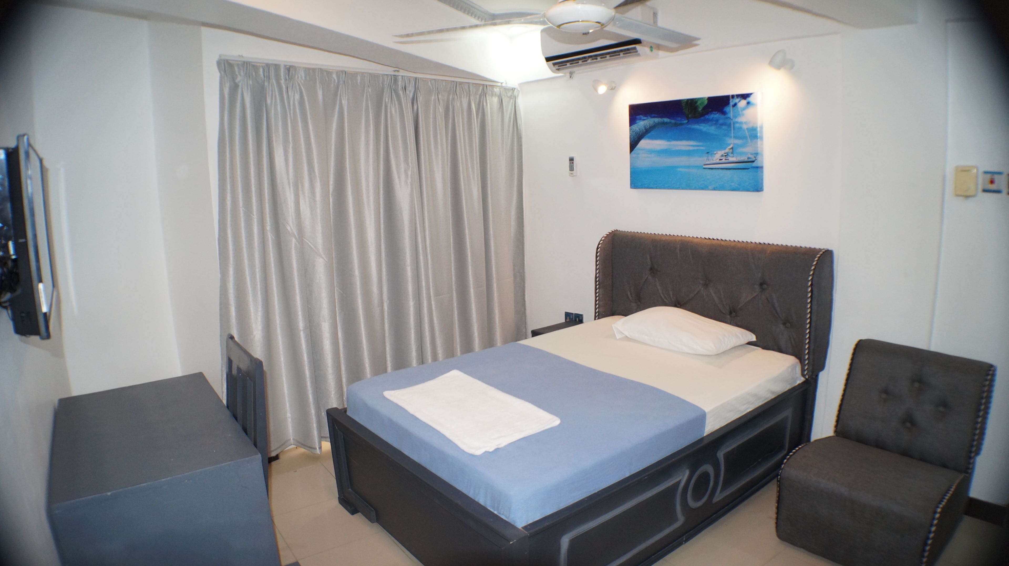 A bedroom with a bed, a chair, a TV, and a painting on the wall.