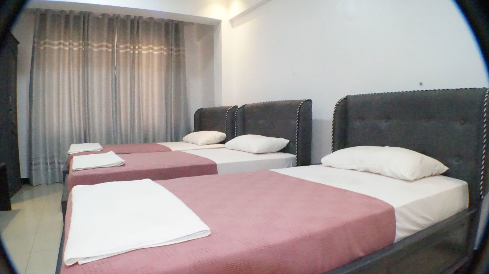 A hotel room with two beds, a window with curtains, and a nightstand.