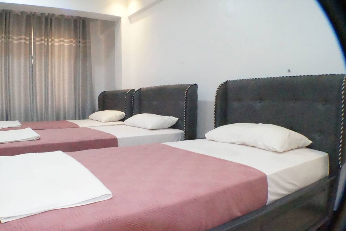 A hotel room with two beds, a window with curtains, and a nightstand.