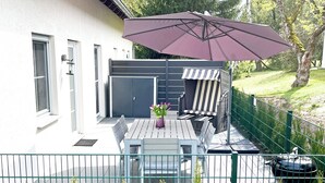 A patio with a table and chairs, a striped outdoor chair, a purple umbrella, and a green fence. - Fantastically situated vacation home for families & dogs, fenced, 200m to Lake Plau (Fünfseen OT Lenz-Süd)
