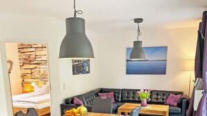 A modern living room with a wooden dining table, black leather sofa, and a stone accent wall. - Fantastically situated vacation home for families & dogs, fenced, 200m to Lake Plau (Fünfseen OT Lenz-Süd)