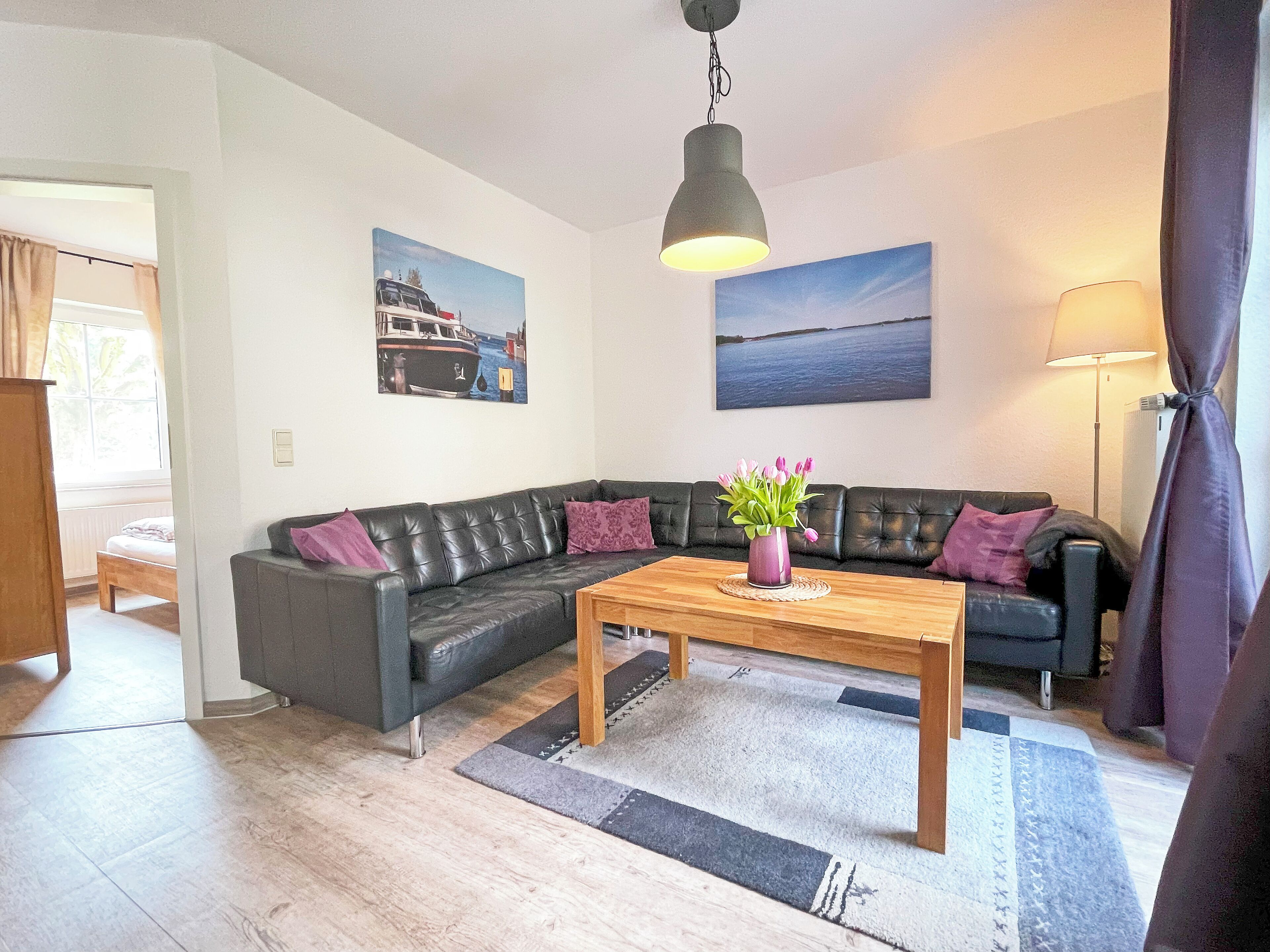 Ein modernes Wohnzimmer mit einem schwarzen Ledersofa, einem Couchtisch aus Holz und zwei Bildern an den Wänden.