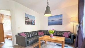 A modern living room with a black leather sectional sofa, a wooden coffee table, and two paintings on the walls. - Fantastically situated vacation home for families & dogs, fenced, 200m to Lake Plau (Fünfseen OT Lenz-Süd)