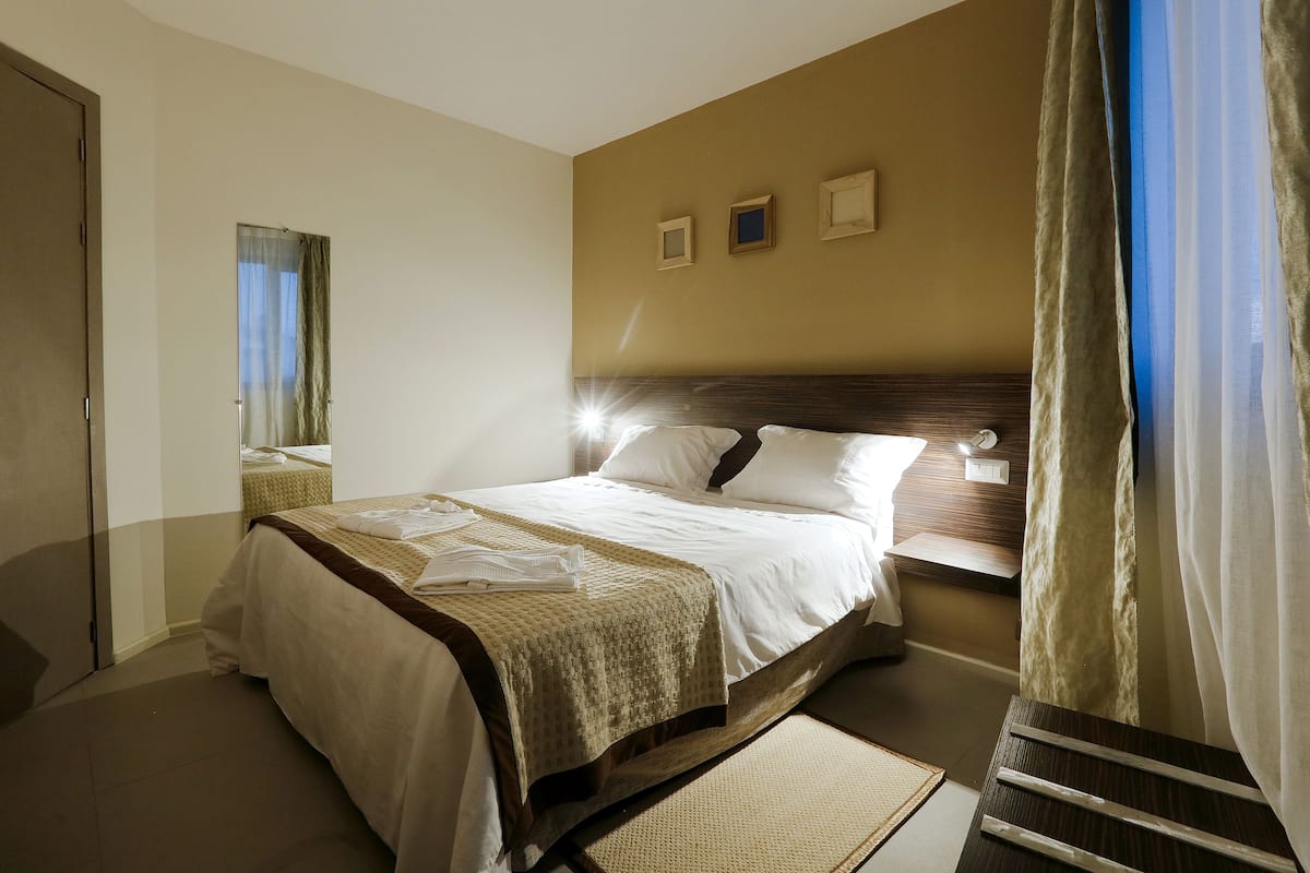 A hotel room with a large bed, a bedside table, a mirror, and a view of the outdoors.