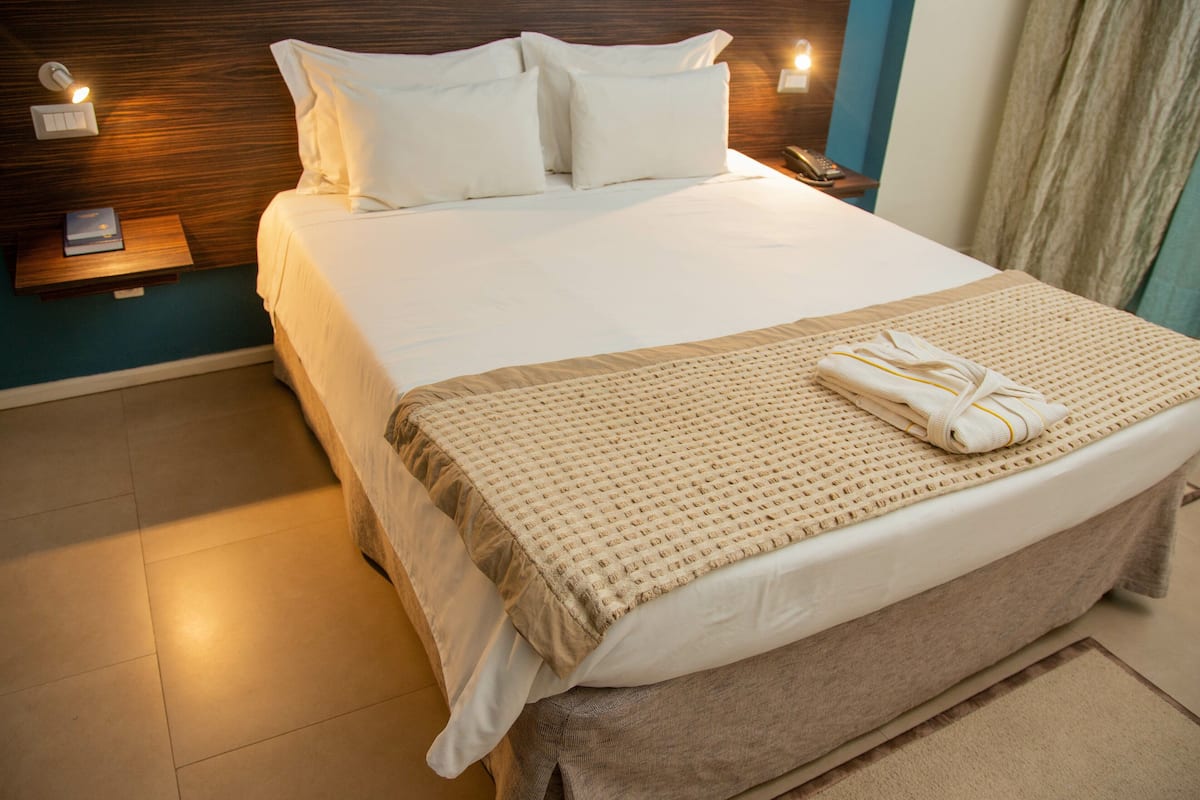 A neatly made bed with white linens, a beige blanket, and a folded towel on the footboard.