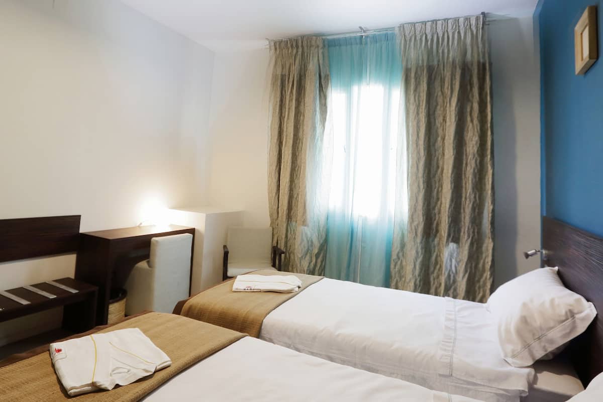 A hotel room with two beds, a desk, a chair, a lamp, and a window with curtains.