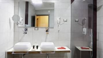 Un baño moderno con dos lavamanos, un espejo grande, ducha y cabina de ducha con paredes de vidrio.