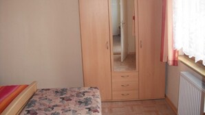 A bedroom with a wooden wardrobe, a bed with a floral bedspread, and a radiator on the wall. - Vacation apartment MAXIM - Holiday apartments (Koserow)