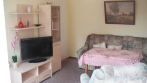A living room with a TV on a stand, a sofa, and a table with a pink tablecloth. - Vacation apartment MAXIM - Holiday apartments (Koserow)