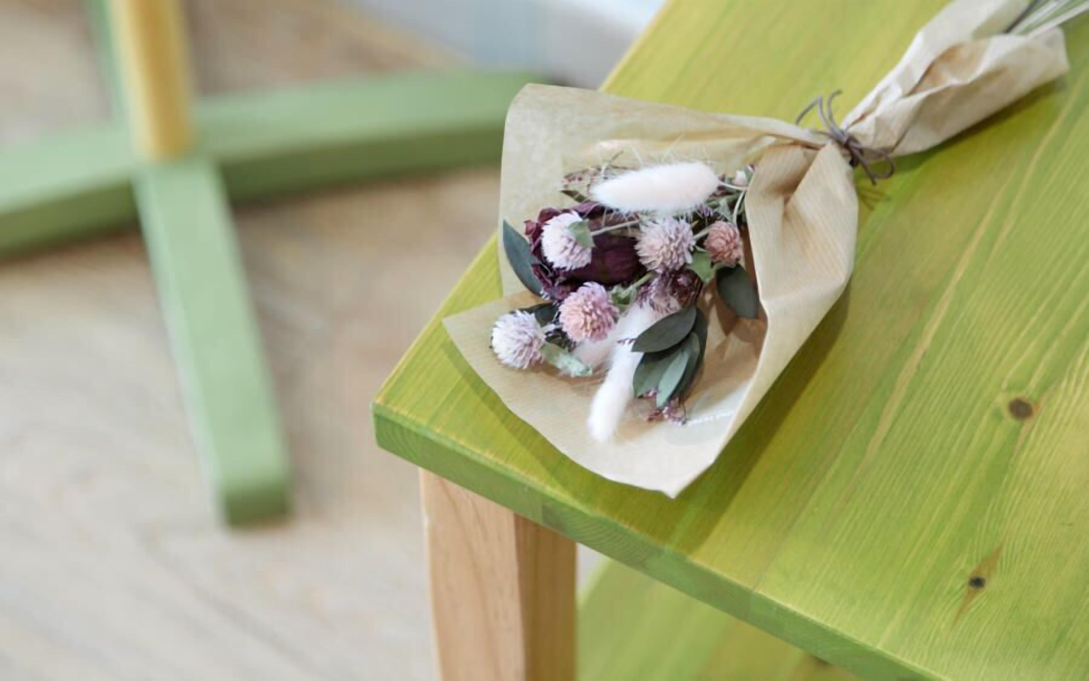 Un ramo de flores envuelto en papel marrón atado con una cuerda, sobre un banco de madera verde.