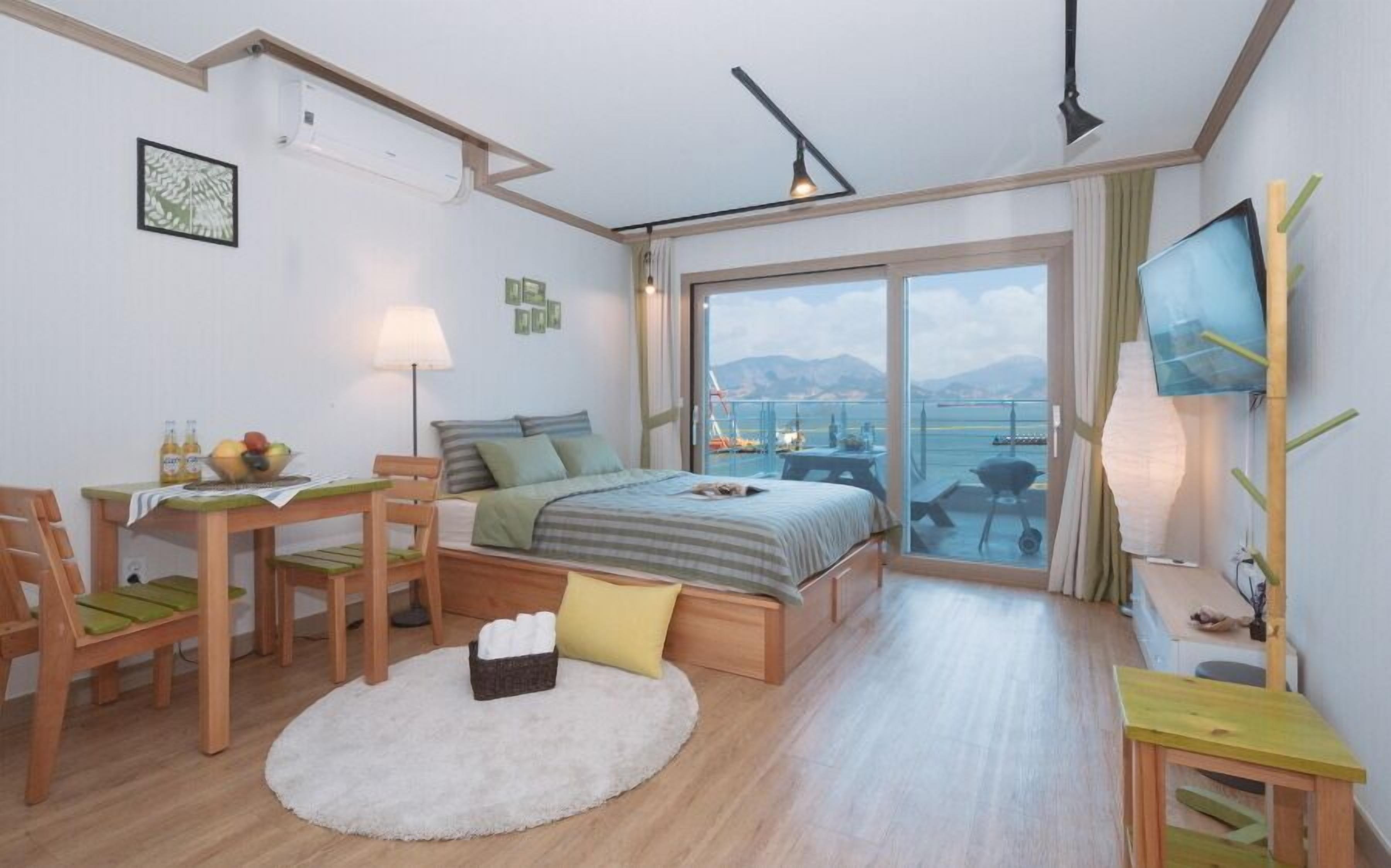 Una habitación de hotel moderna con una cama, un escritorio, una silla, una mesita, un televisor y un balcón con vistas al mar.