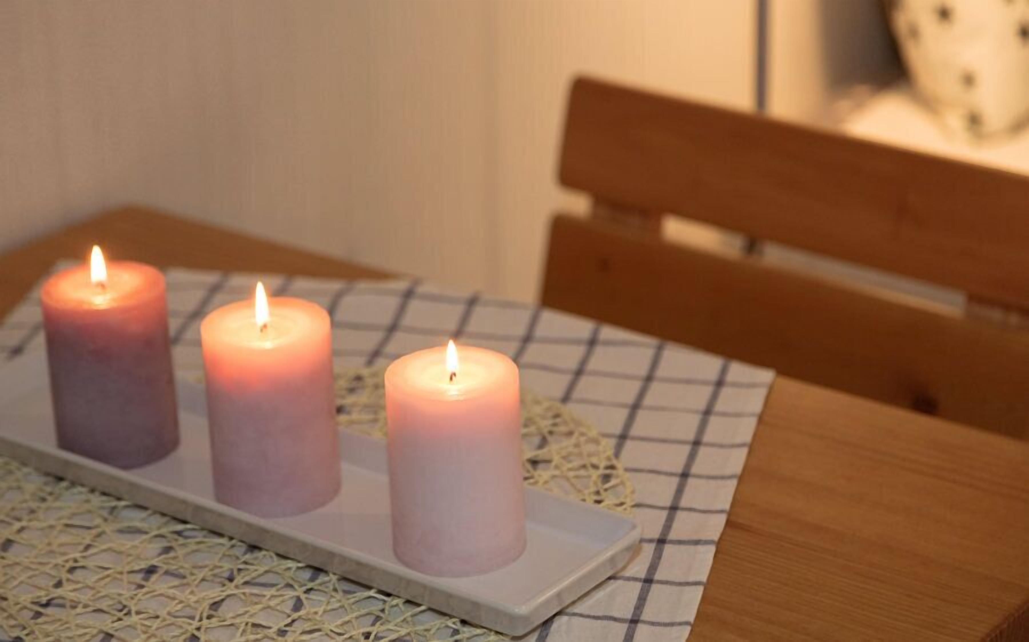 Three lit candles on a white tray on a checkered tablecloth.