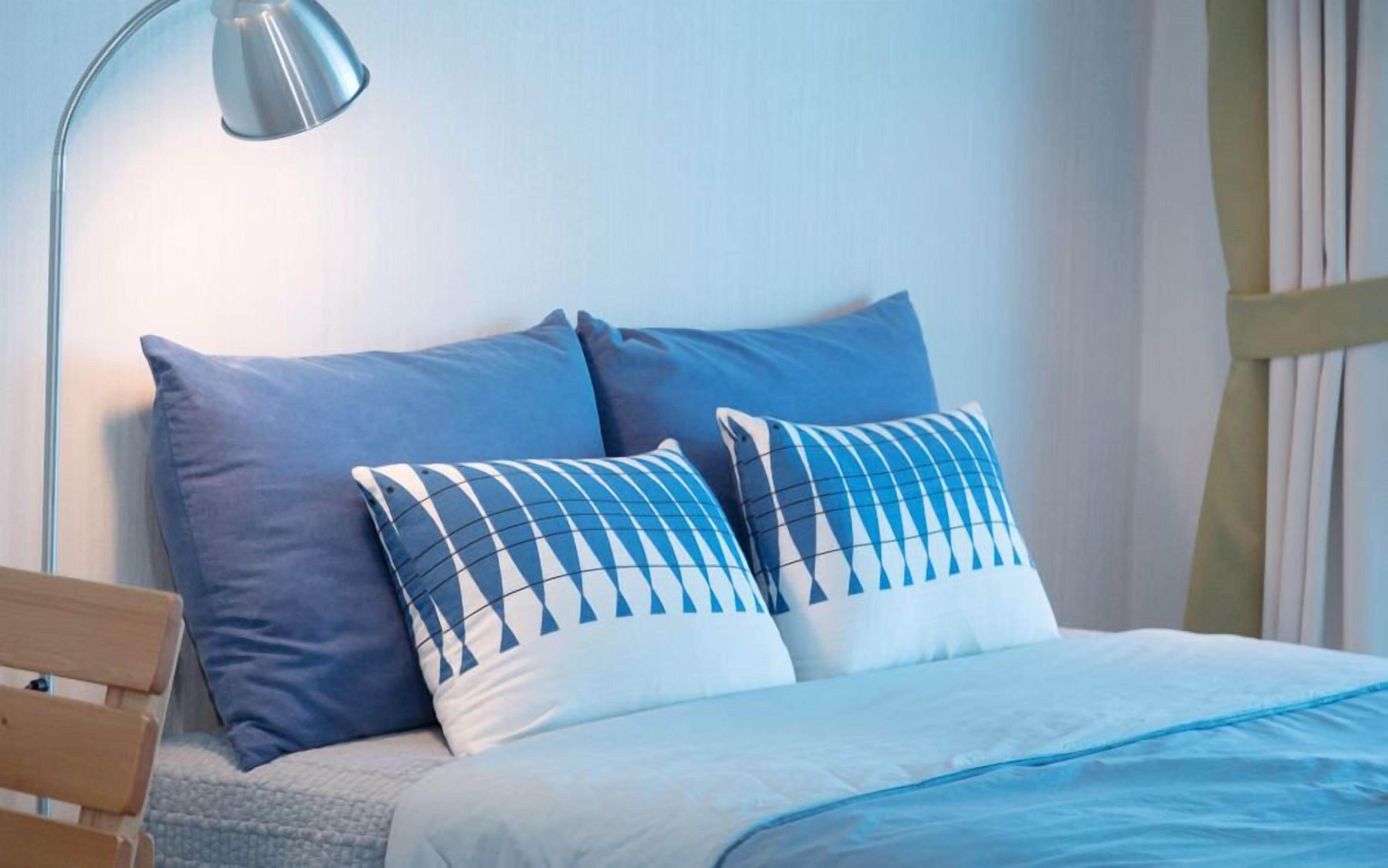 A bed with blue and white pillows, a wooden headboard, and a bedside lamp.
