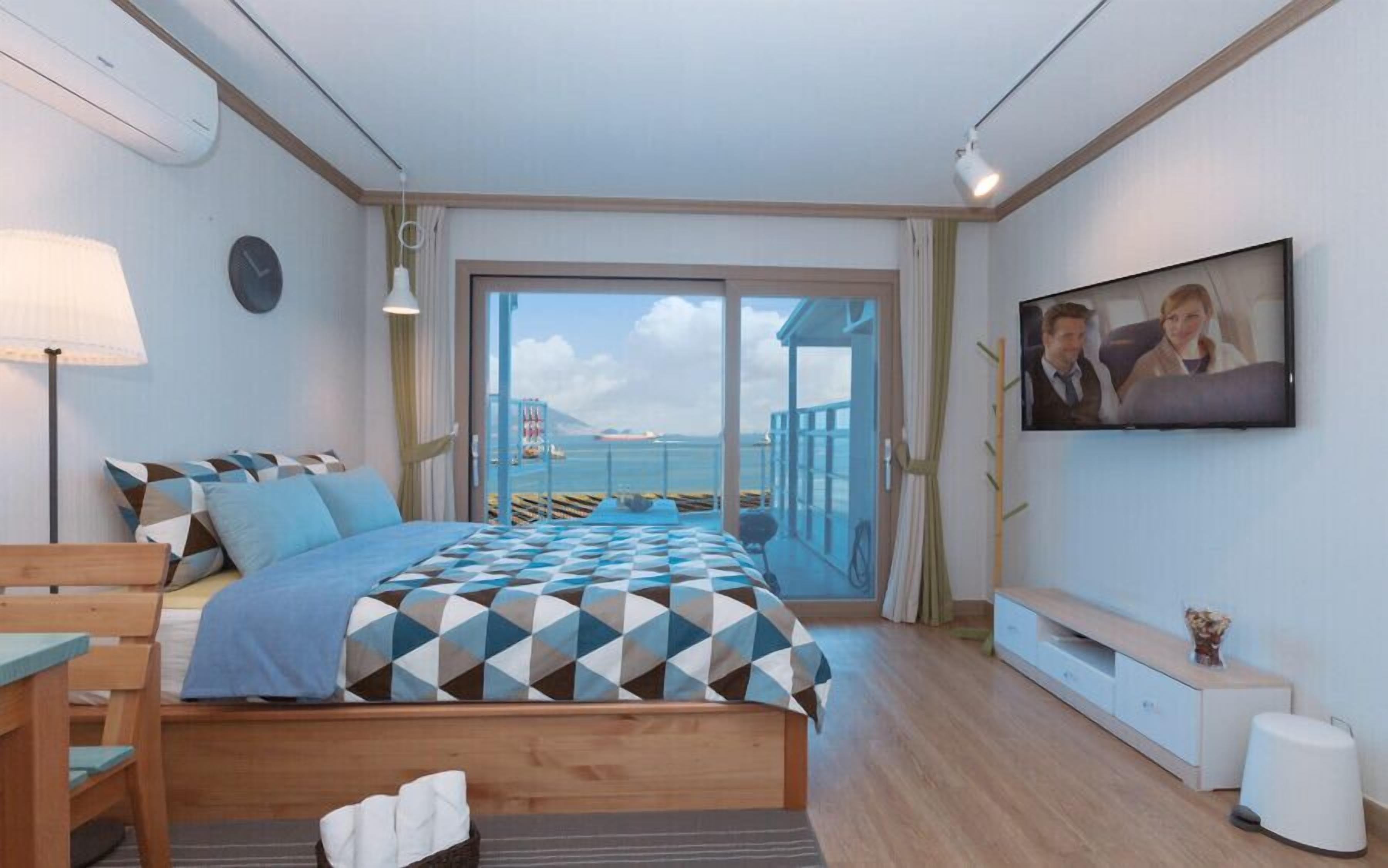 A modern bedroom with a bed, a TV, and a balcony with a view of the sea.