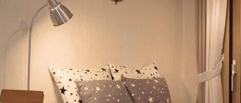 Un dormitorio con cama, almohadas estampadas con motivos de estrellas, un escritorio, una lámpara y un reloj de pared.