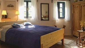 Una camera da letto con un letto in legno, due finestre con tende, uno specchio, un'armadio in legno e una lampada da comodino.