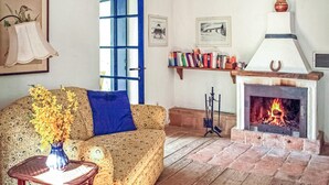 Un soggiorno accogliente con un divano a fantasia, un cuscino blu, un vaso con fiori gialli, un camino e una libreria piena di libri.