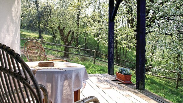 Un pontile in legno con tavolo e sedie, circondato da una ringhiera in legno, con vista su un paesaggio verde e rigoglioso.