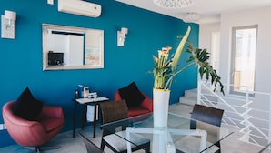 Un salon moderne avec un mur d’accent de couleur turquoise, une table à manger en verre, des chaises rouges et un escalier avec une rampe blanche.