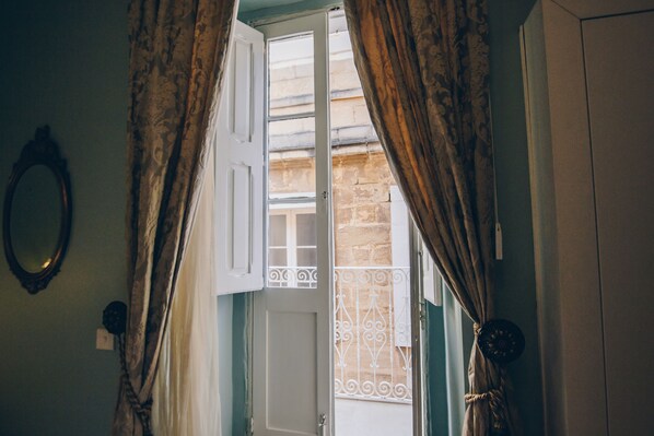 A room with a door leading to a balcony, a mirror on the wall, and curtains. - Sally Port Senglea (Senglea)