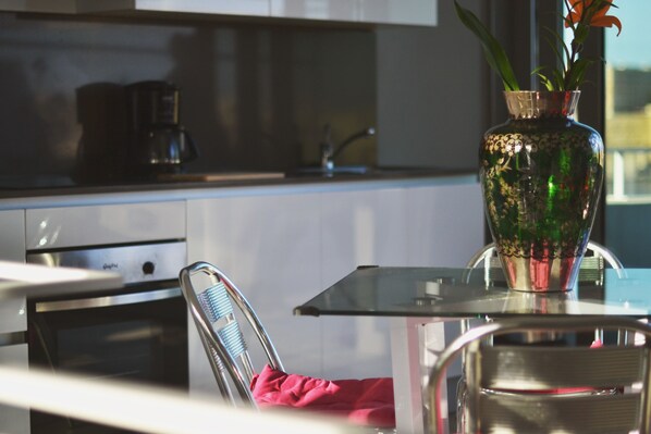 Une cuisine moderne avec une table en verre, des appareils électroménagers en acier inoxydable et un vase décoratif rempli de fleurs.
