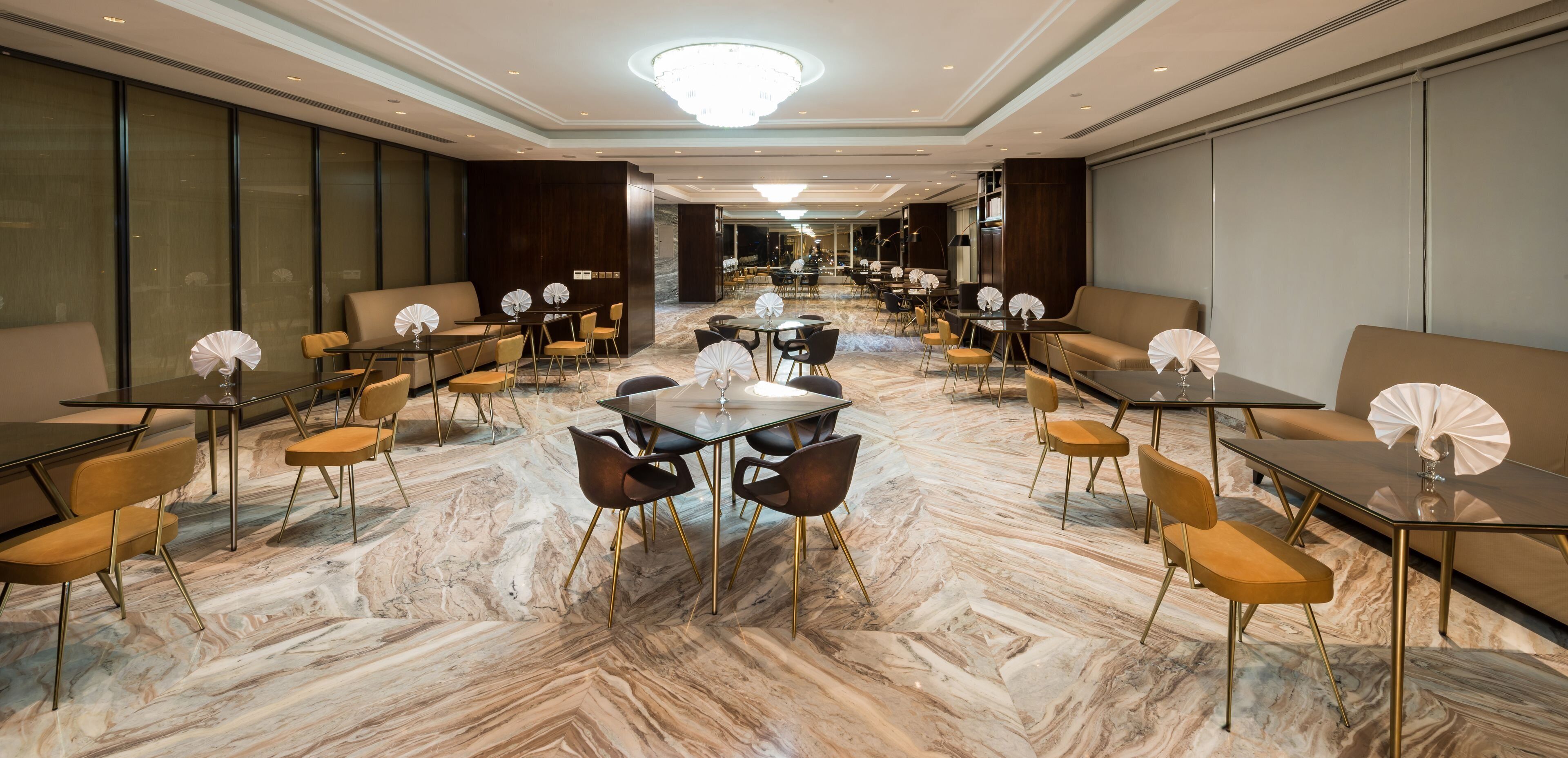 Un hall d’hôtel spacieux, doté d’un sol en marbre, de plusieurs espaces de détente comprenant des canapés et des tables, ainsi que d’un lustre.