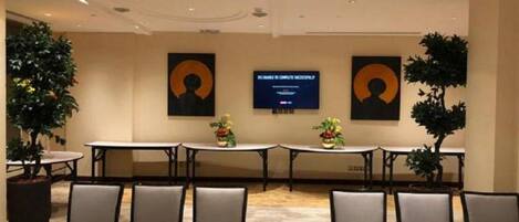 A conference room with tables and chairs, two large screens displaying content, and potted plants.