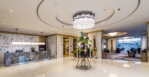 Eine moderne Hotelhalle mit einem Marmor-Rezeptionsschalter, einer zentralen Blumenkomposition und einer großen Chandelier.