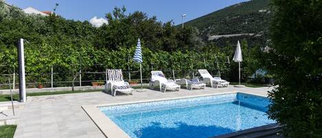 Una piscina con sillas de descanso y sombrillas, rodeada de vegetación y un paisaje montañoso.