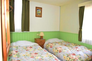 Ein Zimmer mit zwei Betten, jeweils mit floralem Bettbezug, einem Nachttisch aus Holz mit Lampe und einem gerahmten Bild an der Wand.