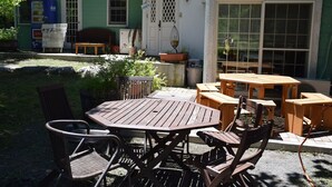 Un patio al aire libre con mesas y sillas de madera, una casa verde al fondo y una máquina expendedora.