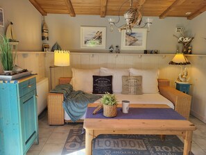 A cozy room with a bed, a wooden table, a wicker chair, a blue cabinet, and a hanging light fixture. - Blue Water 1 - Blue Water 1 (Wustrow)