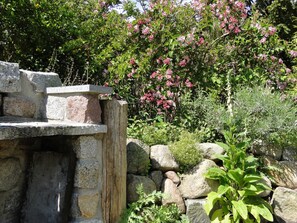 Una estructura de piedra con un poste de madera, rodeada de follaje y plantas en flor.