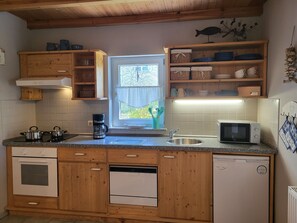 A kitchen with wooden cabinets, a stove, a coffee maker, a microwave, and a window with a view. - Blue Water 1 - Blue Water 1 (Wustrow)