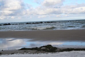 Een strand met golven, een bewolkte lucht en een rij rotsen in het water.