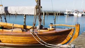 Ein hölzernes Boot liegt an einem Steg, befestigt mit Seilen und einer Winde.