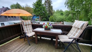 Eine Holzterrasse mit zwei Stühlen, einem Tisch, einer kleinen Tischlampe und einem Blumentopf mit Blumen.