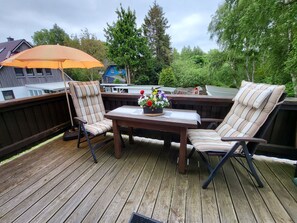 Une terrasse en bois avec deux chaises et une table, une petite lampe de table et une plante en pot ornée de fleurs.