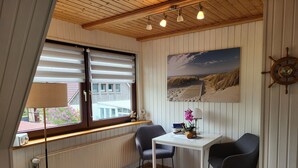 Ein Zimmer mit Holzboden, einem Fenster mit Rollläden, einem Tisch mit Stühlen, einem Bild an der Wand und einer Schiffslenken-Dekoration.