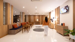 Eine moderne Hotellobby mit einer zentralen Sitzecke, Holzvertäfelung, einem Flachbildfernseher und einer großen Topfpflanze.