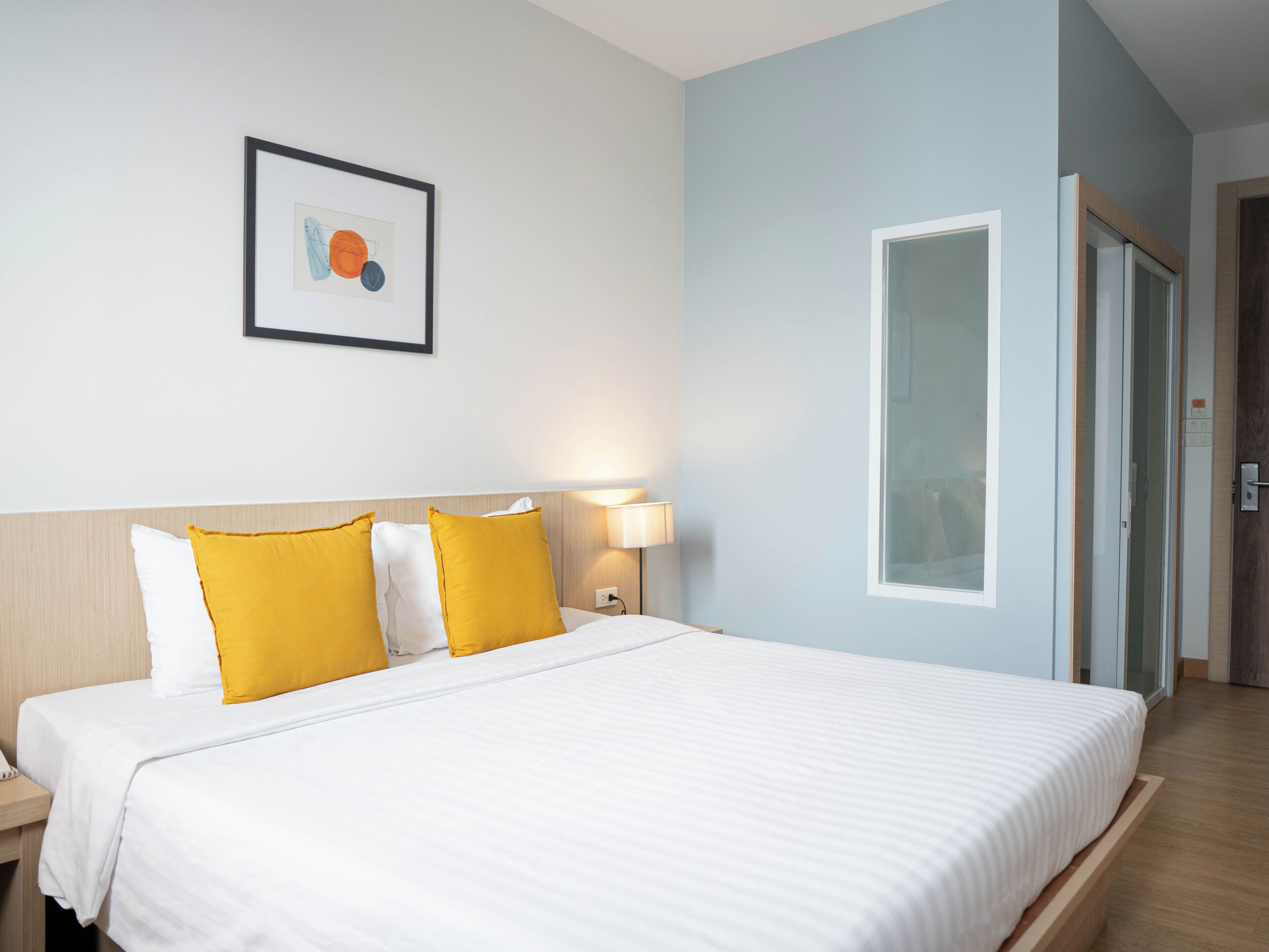 A hotel room with a large bed, a nightstand, a wall-mounted lamp, and a framed picture.