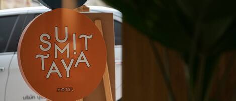Segnaletica di un hotel con la scritta 'Suit M. Taya' e una pianta in vaso sullo sfondo.
